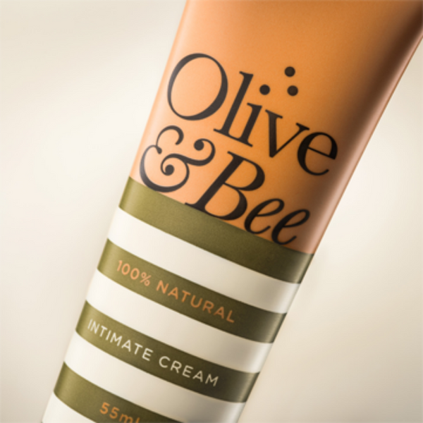 A close-up of a tube of "YES® Olive & Bee Intimate Cream." The packaging is mostly white with horizontal stripes, featuring the brand name in large, elegant font and the words "100% Natural" and "55ml" prominently displayed, perfect for hydrating sensitive skin.