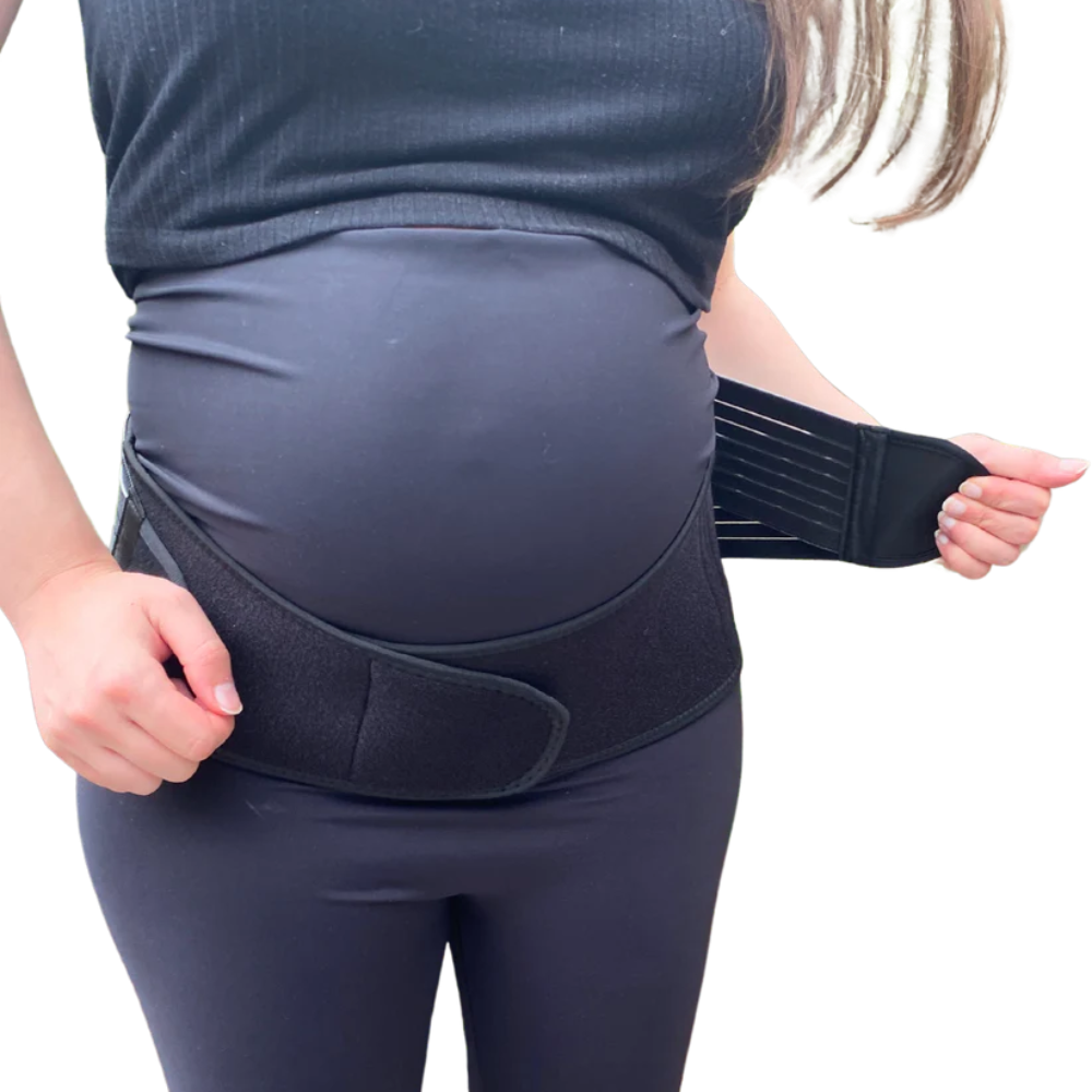 A pregnant woman adjusts the strap of a GRDL Pregnancy Belt by GRDL, worn over her clothes. The image focuses on her torso, highlighting trusted pelvic and back support for pregnancy.