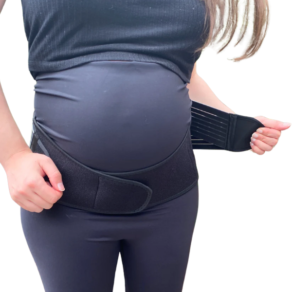 A pregnant woman adjusts the strap of a GRDL Pregnancy Belt by GRDL, worn over her clothes. The image focuses on her torso, highlighting trusted pelvic and back support for pregnancy.