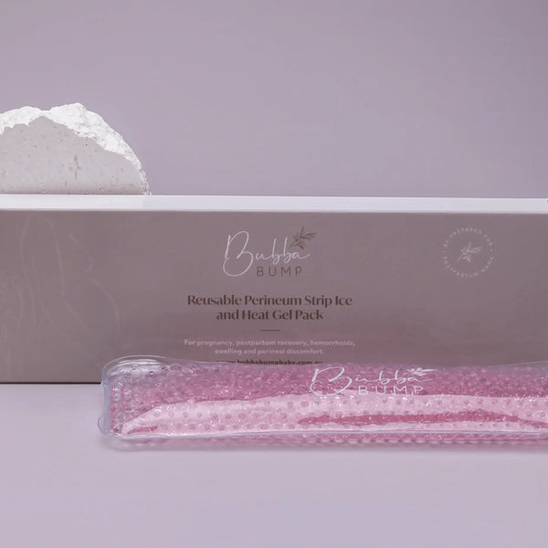 A beige box labeled "Bubba Bump Perineum Ice And Heat Pack" sits alongside a white textured stone and a clear pouch containing a pink gel pack. This perineal ice pack is intended for use during pregnancy, postpartum recovery, vaginal birth, hemorrhoids, swelling, and perineal discomfort.