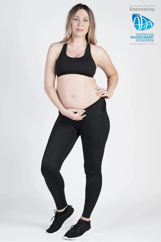 A pregnant woman is standing and smiling at the camera, dressed in a black sports bra, SRC Maternity Leggings by SRC Health in black, and black sneakers. Her left hand supports her belly while her right hand rests on her hip. The image is endorsed by the Australian Physiotherapy Association.