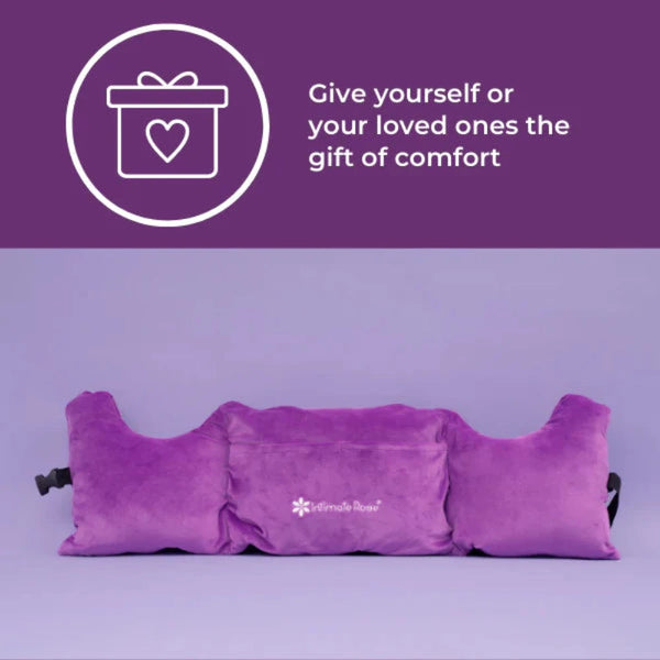 Against a purple background, the Post-Surgery Mastectomy Pillow from Intimate Rose is shown with armrests. In the top left corner, a white gift icon with a heart is accompanied by the text: "Give yourself or your loved ones the gift of comfort.