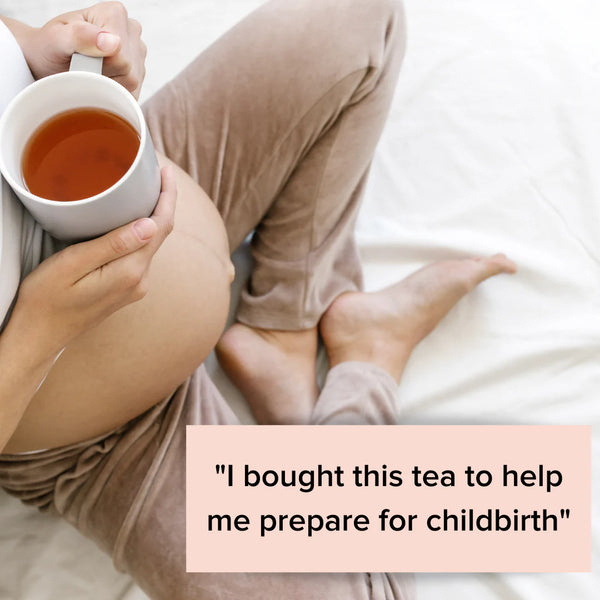 A pregnant person sits on a bed, holding a mug of The Breastfeeding Tea Co's Pregnancy Tea - Raspberry Leaf Tea. They are wearing comfortable beige pants and a white top. A text box in the image reads, "I bought this Pregnancy Tea to help me prepare for childbirth with pregnancy safe herbs.
