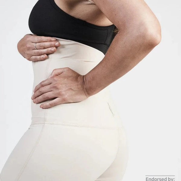 A woman wearing a black sports bra and the SRC Recovery Short - Mini in beige, from SRC Health, is shown in a side profile view with her hand placed on her back to emphasize postpartum recovery. The image is endorsed by the Australian Physiotherapy Association, as indicated by their logo in the lower right corner.