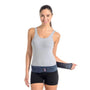 A woman in a gray tank top and black shorts demonstrates wearing the Serola Belt - Pregnancy Sacroiliac Belt by Serola, fastening the Velcro strap around her hips for SI joint support and lower back pain relief while smiling at the camera.