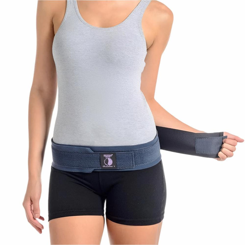 A woman in a gray tank top and black shorts demonstrates how to wear the Serola Belt - Pregnancy Sacroiliac Belt by Serola. Smiling at the camera, she holds one end of the belt in her right hand against a white background.