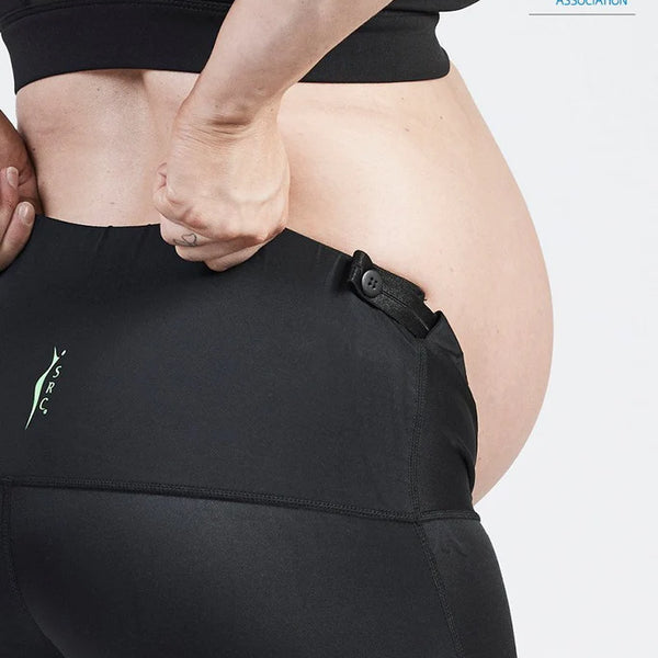 A close-up of a pregnant person wearing the SRC Maternity Shorts from SRC Health. They adjust the waistband that provides pelvic support, with a visible endorsement by the Australian Physiotherapy Association in the top right corner, highlighting low back pain relief during pregnancy.