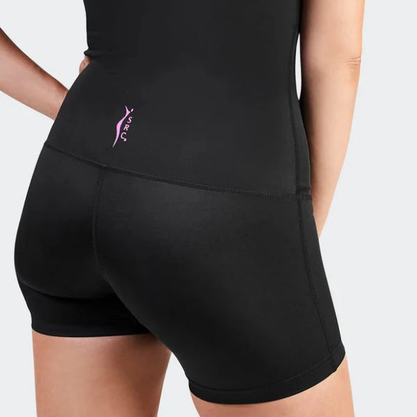 A person wearing the SRC Health's fitted black athletic outfit, specifically the SRC Recovery Short - Mini, designed for medical-grade compression. The shorts feature a small purple logo on the left side. With their left hand resting on their hip and facing away, they stand against a light gray background.