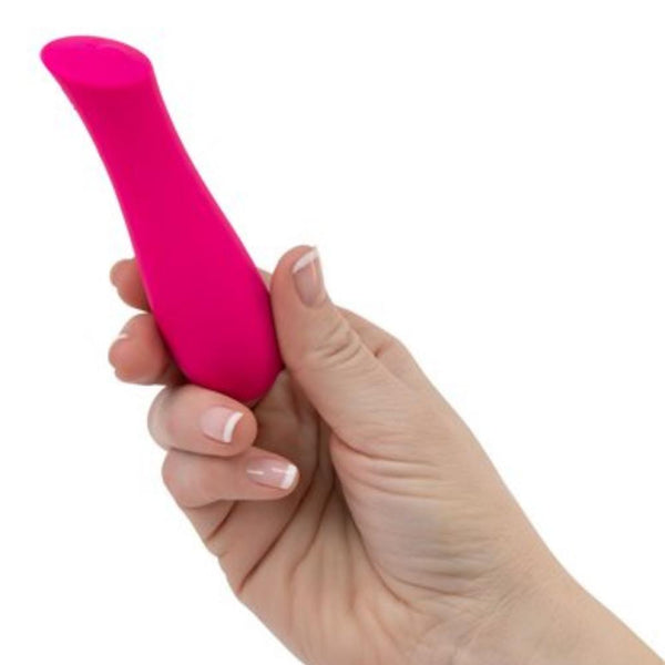 A hand with a French manicure holding "The Mini Swan Rose" by Amielle, a small, pink, cylindrical object with a tapered end made from 100% seamless silicone. The background is plain white.