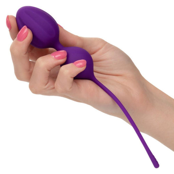A hand holds a set of Calexotics Kegel Weights, featuring three purple exercise balls made from body-safe silicone with retrieval cords. The person's pink-painted nails add an elegant touch, ideal for enhancing pelvic floor muscles during Kegel training.
