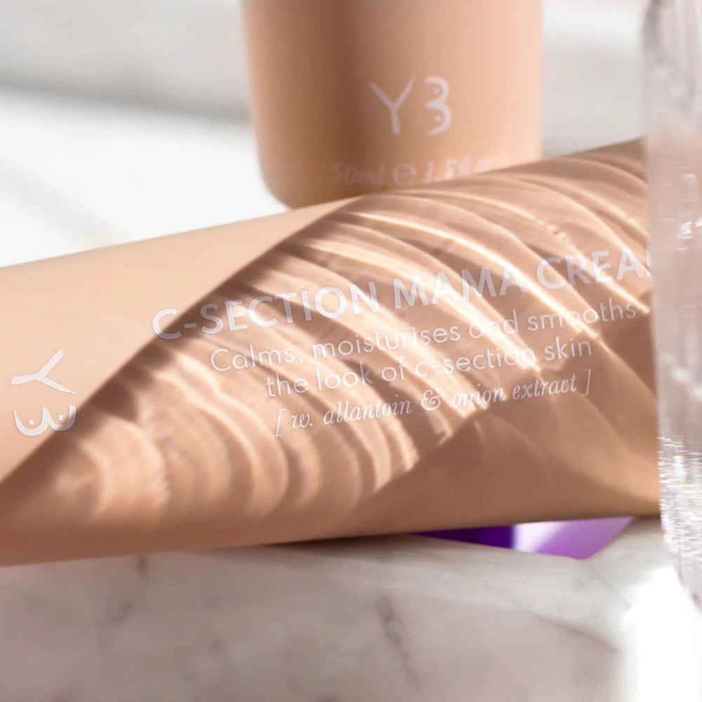 A close-up of a beige tube labeled "C-Section Mama Cream," showcasing its purpose for scar softening using natural ingredients. The tube, featuring a subtle swirl pattern in the background, reads: "Calms, moisturizes and smooths the look of c-section skin [w/o allantoin & onion extract]." The brand logo "Yung Bod" is prominently displayed on the tube.